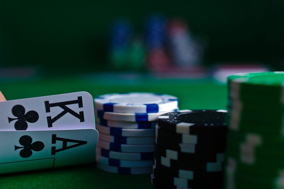A hand holding playing cards beside stacks of poker chips on a green table