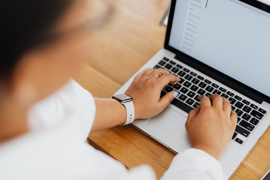 Person typing on a laptop keyboard at a wooden desk while filling in an online account form