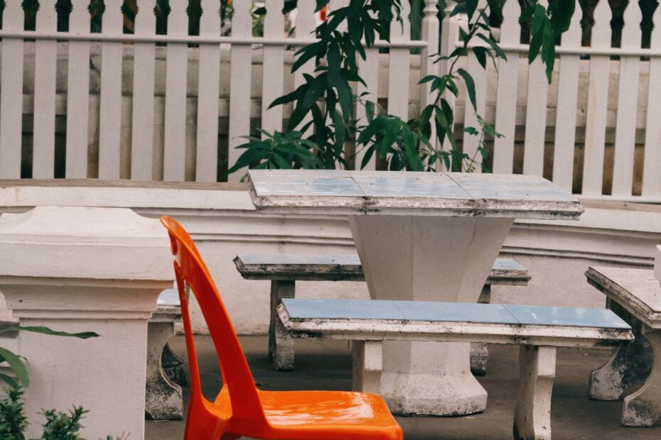 A single orange chair pulled up to a weathered stone table in a garden, a picture of the lone first seat to act in poker