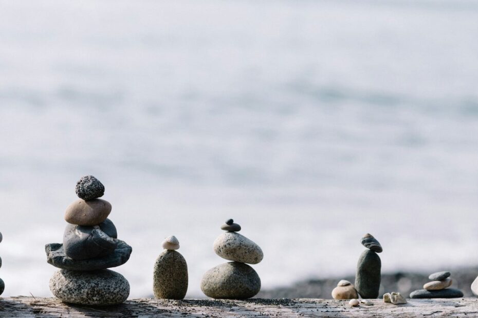Small stacks of balanced stones on a driftwood log in front of calm water, a symbol of staying composed at the poker table