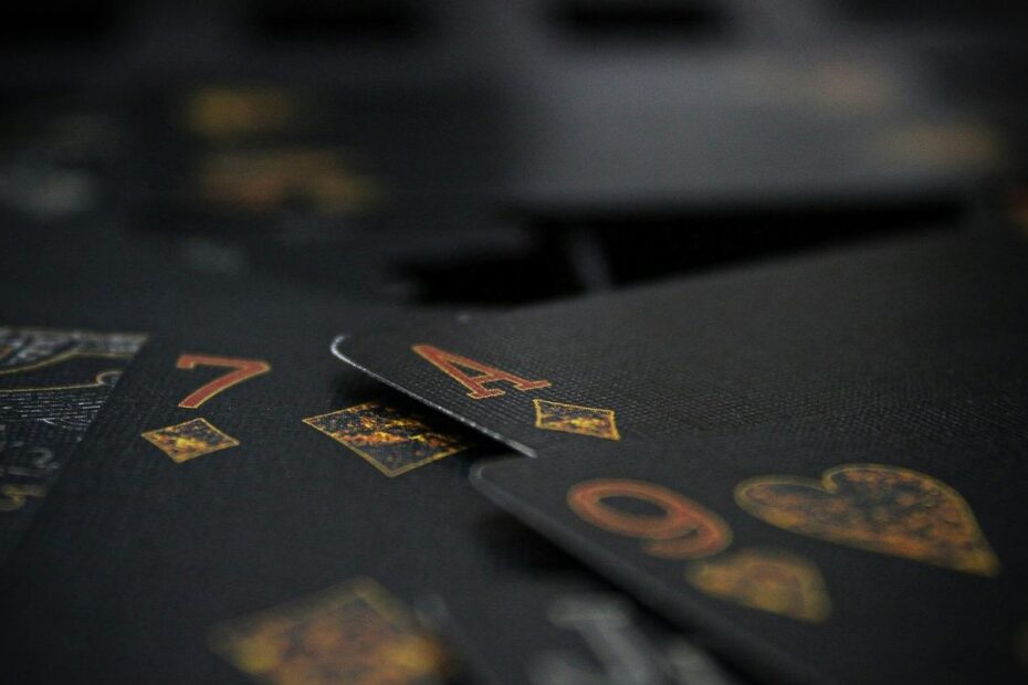 Close-up of black playing cards with gold and red markings, an ace, a seven and a nine, fanned across a dark table
